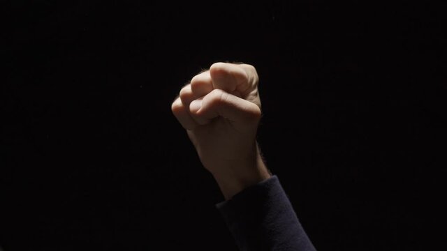 Clenched fist hand raises up in air on black background - sign of protest resist