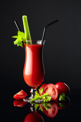 Tomato juice with celery on a black reflective background.