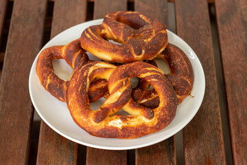 Simple traditional salted home made Pretzel on a white plate set on brown wooden boards top view