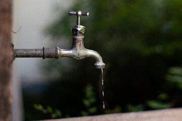 Old rusted metal water faucet with dripping water outside isolated with shallow depth of field...