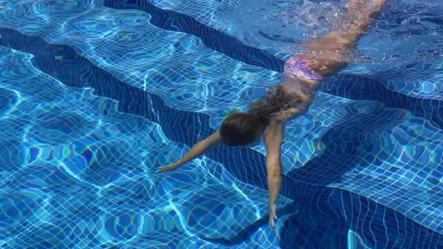 Young girl swimming underwater in blue pool