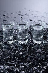 Damp glasses of vodka with ice on a black reflective background.