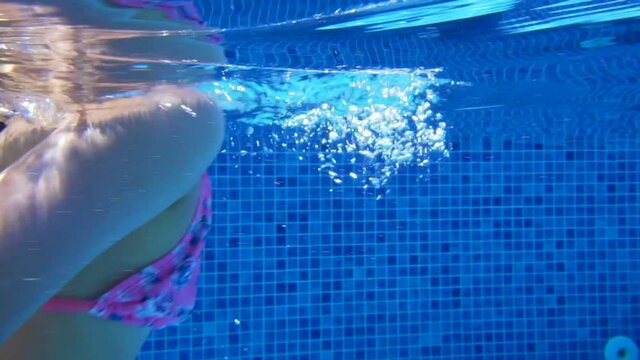 Young girl swimming underwater in blue pool