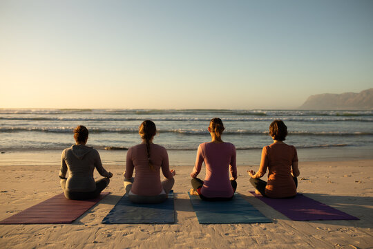 Rear view of women doing yoga on beach