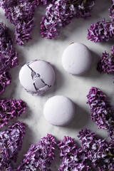 Purple macaroons with lilac flowers on a light marble background, top view