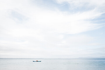 Fototapeta na wymiar A man using a blue Kayak in the Ocean on a still but cloudy day