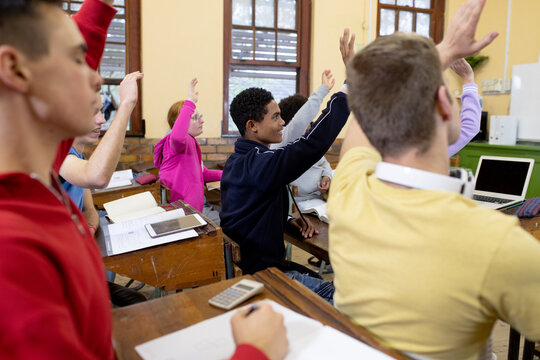 Side view of students raising their hands in class