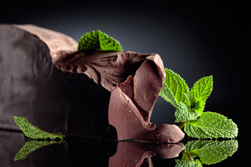 Piece of dark bitter chocolate with mint on a black reflective background.