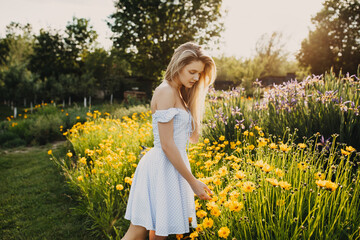 Young woman with long blonde hair, wearing country style dress, in the field of yellow flowers in golden hour.