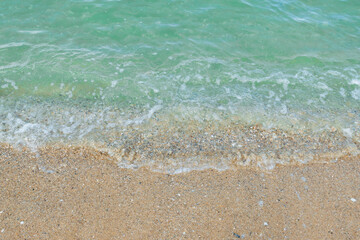 Fototapeta na wymiar Soft wave of emerald ocean on sandy beach for background.