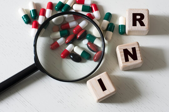 INR (International Normalized Ratio) - a word on cubes on a light background with a magnifying glass and tablets