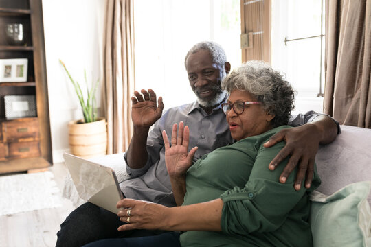 A senior African American couple waving at the laptop and smiling