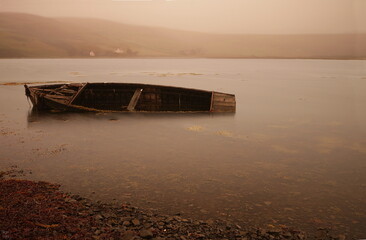 Abandoned boat lies rotting on the shore line, flooded and old beside a fishing lake.