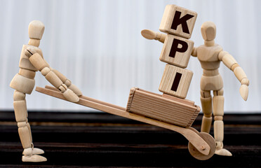 KPI - acronym on cubes standing in wheelbarrow. A wooden man passes them to the second person.
