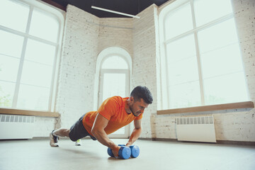 Dumbbell. Young caucasian man training at home during quarantine of coronavirus outbreak, doing exercises of fitness, aerobic. Staying sportive during insulation. Wellness, sport, movement concept.