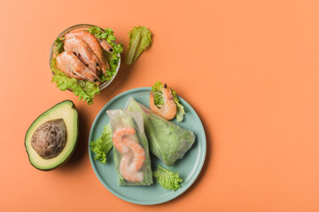Spring rice paper roll with shrimp, avocado, paprika, lettuce and cottage cheese on a bright plate on an orange background.