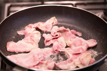 Bacon cooking in a frying pan. Close up with out of focus elements
