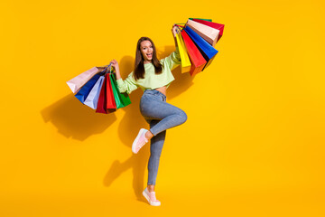 Full body photo of ecstatic crazy girl enjoy shopping achieve buy 50 sales raise bags scream yeah wear green style stylish trendy clothes isolated yellow color background