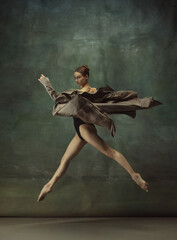 In flight. Graceful classic ballerina dancing, posing isolated on dark studio background. Stylish trench coat. Grace, movement, action and motion concept. Looks weightless, flexible. Fashionable.