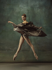 In flight. Graceful classic ballerina dancing, posing isolated on dark studio background. Stylish trench coat. Grace, movement, action and motion concept. Looks weightless, flexible. Fashionable.