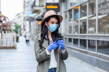 Fototapeta premium Portrait of a young woman wile wearing a face mask for protection from cold and flu and viruses. Young woman with face mask in the street. Woman wearing face mask because of air pollution in the city