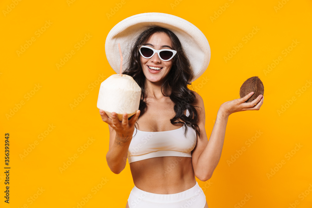 Wall mural image of smiling young woman in swimsuit and hat holding coconuts