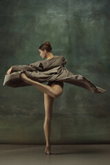 Fototapeta premium Warm. Graceful classic ballerina dancing, posing isolated on dark studio background. Stylish trench coat. Grace, movement, action and motion concept. Looks weightless, flexible. Fashionable, style.
