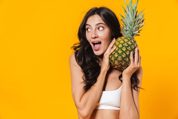 Image of excited brunette woman holding pineapple and looking aside