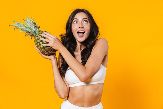Image of excited brunette woman holding pineapple and looking upward