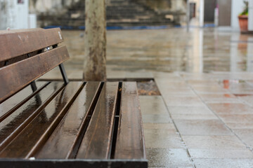 Fototapeta na wymiar Wooden bench in city center on rainy day