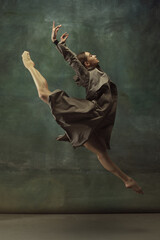 In flight. Graceful classic ballerina dancing, posing isolated on dark studio background. Stylish trench coat. Grace, movement, action and motion concept. Looks weightless, flexible. Fashionable.