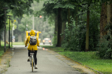 One unrecognizable person with yellow oilskin on bike riding through rainy street in beautiful old...
