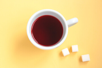 Red hibiscus tea in a white cup with sugar cubes isolated on a light orange background. Selective focus. Top view
