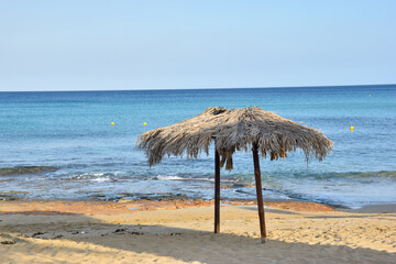 Fototapeta na wymiar Two lonely straw beach umbrellas on an empty sandy beach, sea, blue sky
