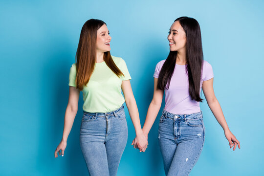 Photo of charming positive two people ladies lesbians couple hold arms walking street chatting best buddies fellowship wear casual green violet t-shirts jeans isolated blue color background