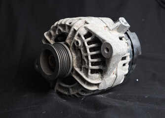Used, dirty unclean alternator car part shot on a black background to highlight the silver metal piece of a car taken to be replaced with a brand new part. Pulley an electric parts discarded rubbish