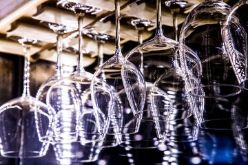 Transparent wine glasses hang down in the bar or restaurant or cafe. Close-up. Selective focus. Abstract background.