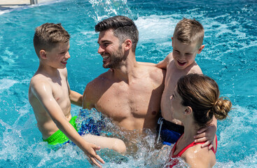 Smiling family of four having fun and relaxing in outdoor swimming pool at hotel resort.