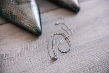 Silver shoes with a pendant on a wooden surface close up