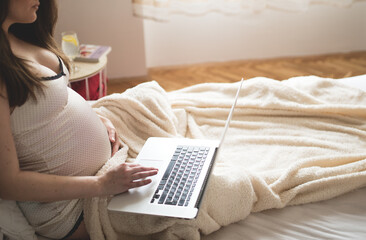 Lovely pregnant woman relaxing with her laptop while lying on a bed at home