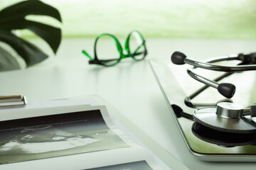 statoscope and tablet computer on a white table, online medical consultation, leaf of a tropical monstera plant, light green nice background