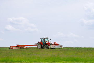 Fototapeta na wymiar Big red tractor with two mowers mows the grass for silage