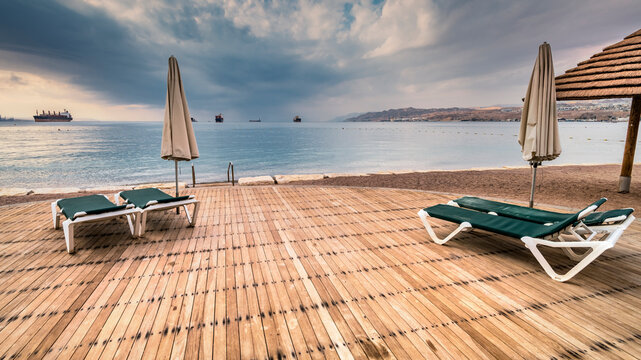 Deck chairs on wooden floor and umbrella on tropical beach