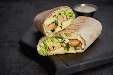 Wrap with fried chicken, vegetables and sauce isolated on dark  background