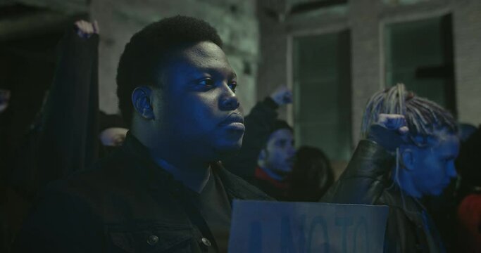 Crop view of afro american man holding placard while standing in crowd of protesters at night street. Strike against police brutality, racism and fatal use of force by officers