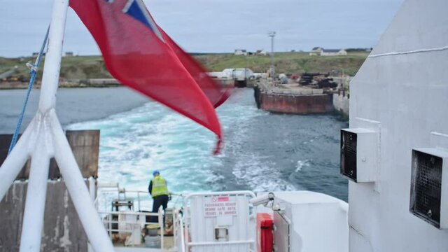 View from the back of a ferry leaving the coast of north scotland. Union jack flattering in the wind