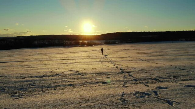 Man walking alone in the snow during sunset. Tracking shot