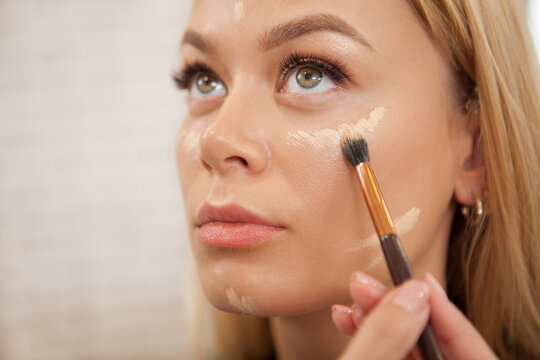Close up of a makeup artist applying liquid concealer or highlighter on the face of female client