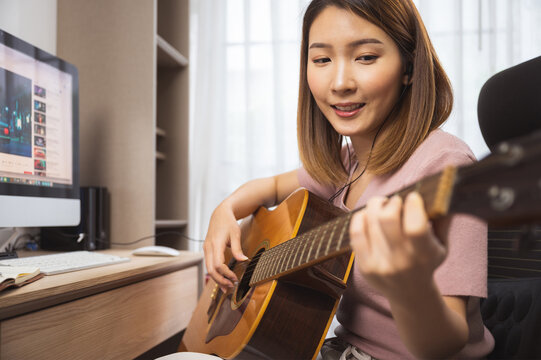 Asian Woman Guitar Player And Vlogger Playing Guitar In Front Computer At Home While Social Distancing Of Coronavirus Outbreak, Online Guitar Lesson,livestream On Social Media Concept.