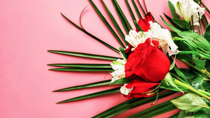 A bouquet of red roses with white flowers and a palm leaf on a pink background.